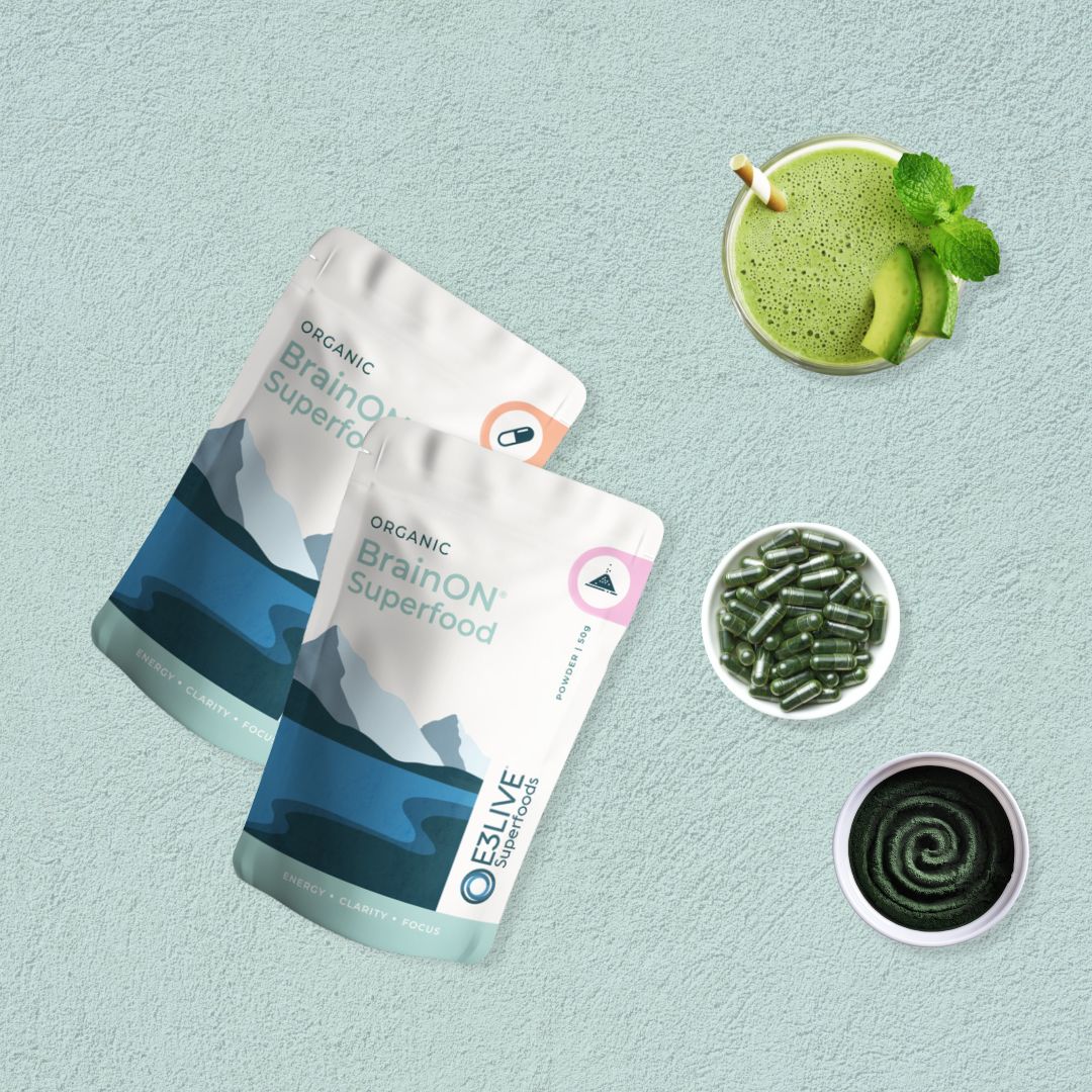 Two packs of BrainON® Superfood, one labeled for capsules and the other for powder. Surrounding the packs are a vibrant green smoothie with avocado and mint garnish, a bowl of green capsules, and a swirl of green powder showcasing the nutrient-rich BrainON® products.